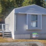 Gray mobile home with white porch steps and a "FOR SALE" sign in the front yard.