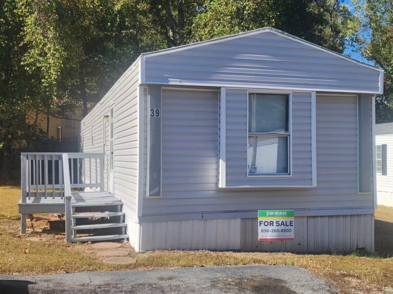 Gray mobile home with white porch steps and a "FOR SALE" sign in the front yard.