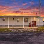 Single-wide mobile home with covered porch and red stairs at sunset.