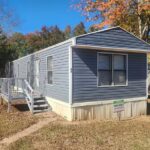Blue single-wide mobile home with a small front porch and stairs, surrounded by autumn trees.