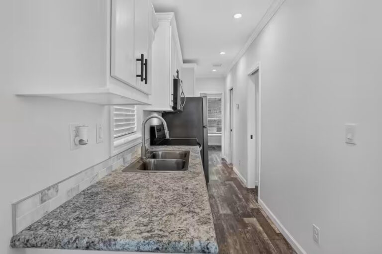 Galley kitchen with granite countertop, stainless sink, white cabinets, and black refrigerator