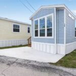 Blue and white mobile home with bay window, numbered 119, next to a yellow mobile home.