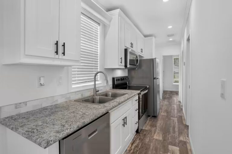 White galley kitchen with granite counters, stainless appliances, wood-look floors