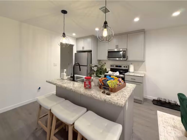 Modern kitchen with gray cabinets, granite island, pendant lights, and white barstools