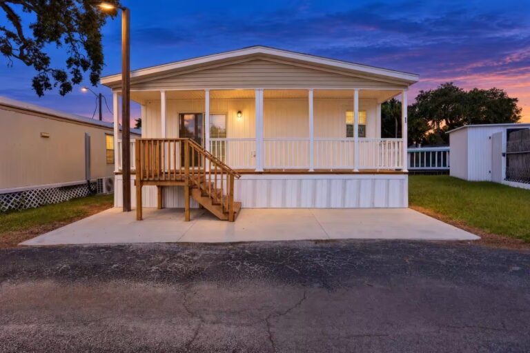 White mobile home with covered porch and wooden stairs under a colorful sunset sky