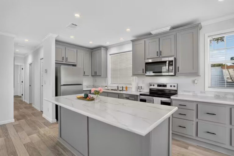 Modern kitchen with gray cabinets, white marble island, and stainless steel appliances.