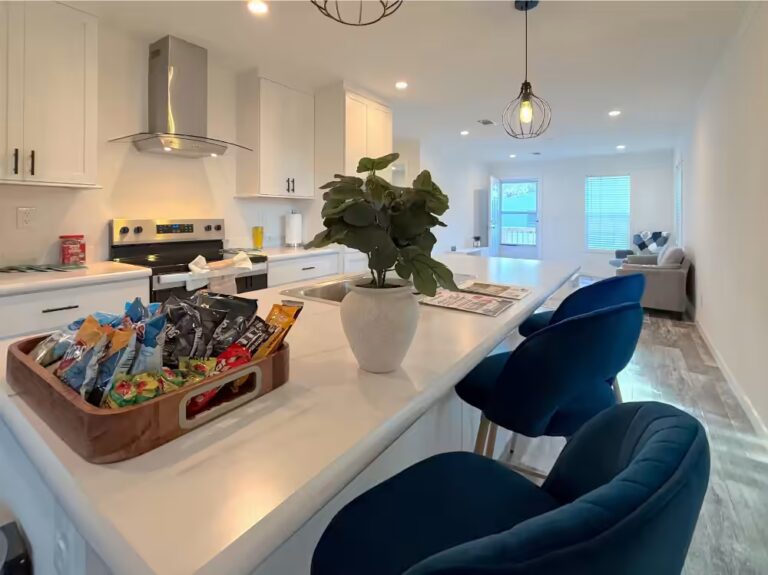 White kitchen island with navy blue velvet bar stools, snack tray, and potted plant.