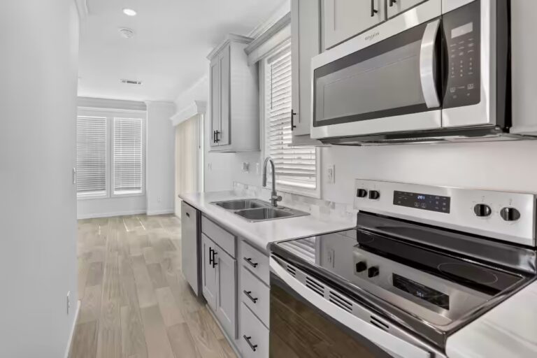 Modern kitchen with white cabinets, stainless steel microwave, stove, sink, wood-look floors.