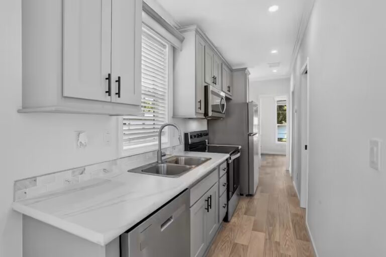 White galley kitchen with stainless steel appliances, marble countertops, and wood-look flooring