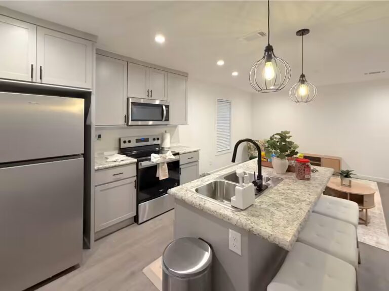 Modern kitchen with white cabinets, stainless steel appliances, granite island, and pendant lights