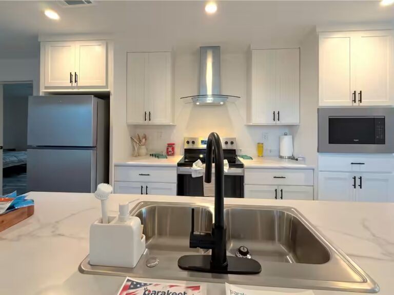 White kitchen with stainless appliances and double sink with black faucet; paper reads Barakool