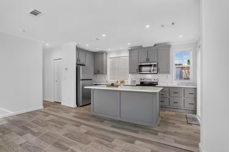 Modern kitchen with gray cabinets, white island, stainless steel appliances, and wood-look flooring.