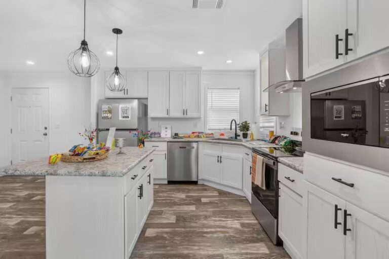 Modern white kitchen with granite counters, stainless appliances, island, and pendant lights.