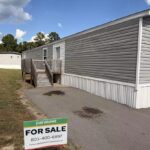 For Sale sign: parakeet, 803-400-6897, in front of gray manufactured home