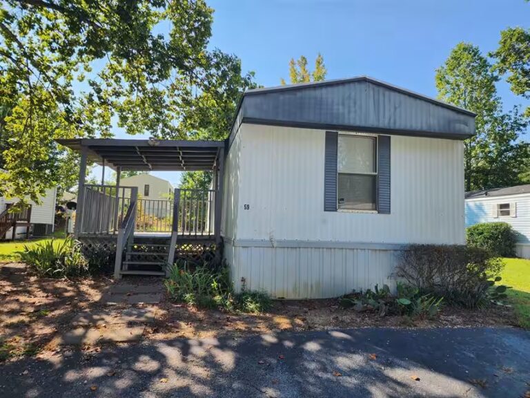 White mobile home with covered porch, number 58, surrounded by trees