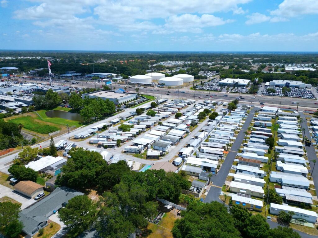 Aerial view of a large mobile home park beside a busy highway, with white storage tanks in the distance.