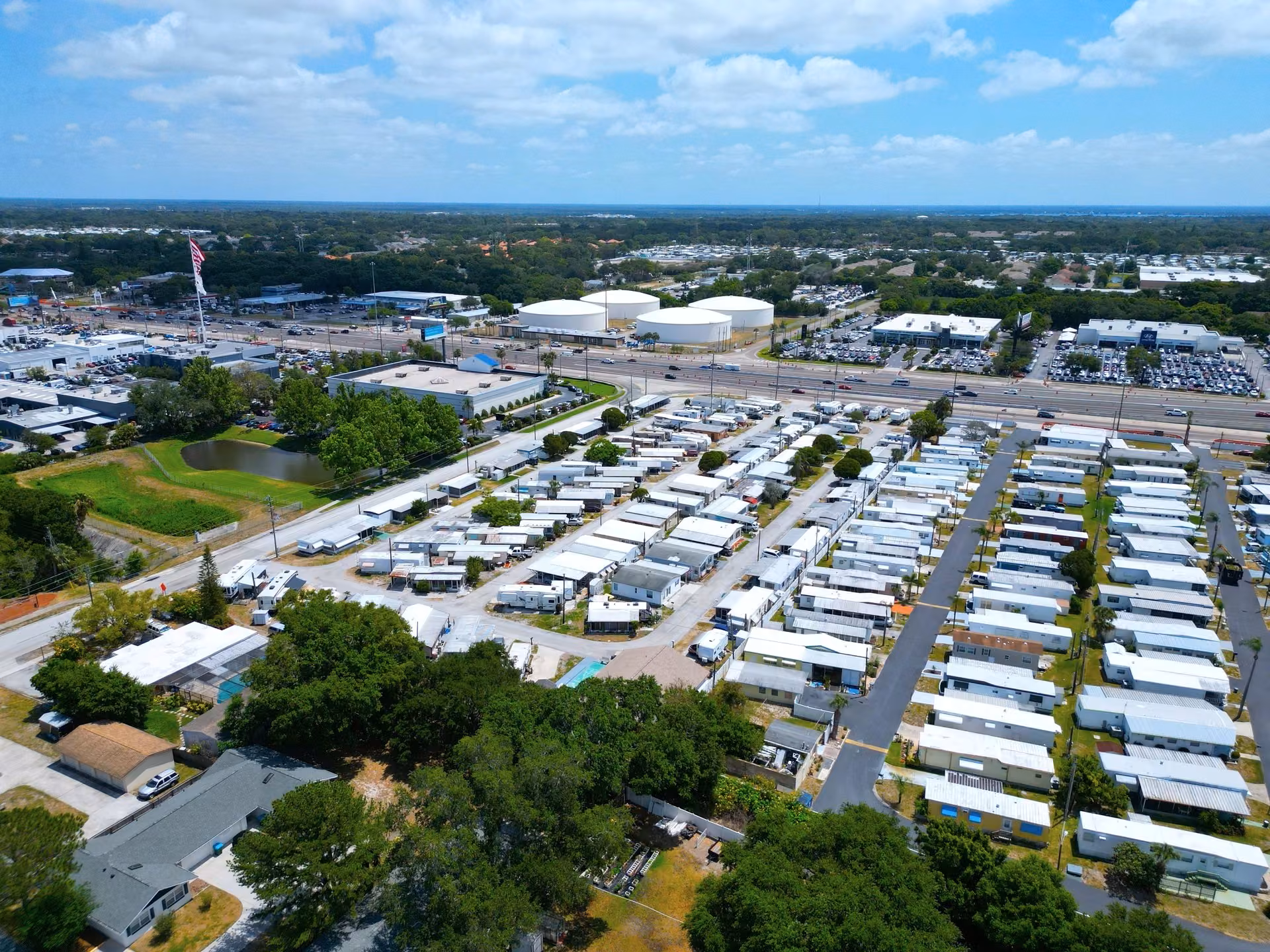 Aerial view of a large mobile home park beside a busy highway, with white storage tanks in the distance.