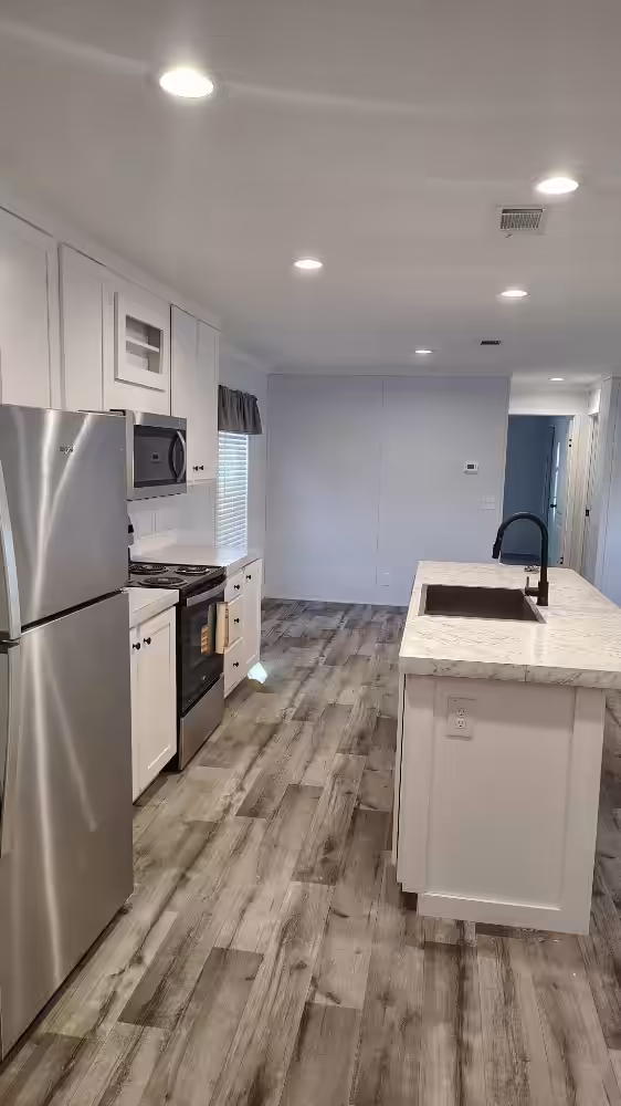 Modern kitchen with white cabinets, stainless appliances, island with sink, and weathered wood-look flooring.