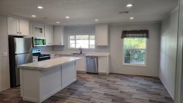 Bright kitchen with white cabinets, marble island, stainless appliances, and wood-look flooring.