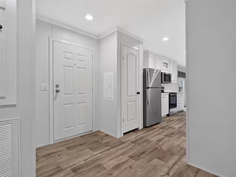 White entryway with two panel doors, wood-look flooring, and kitchen with stainless fridge