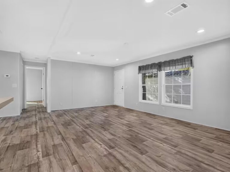 Empty room with wood-look flooring, gray walls, two curtained windows, and white door