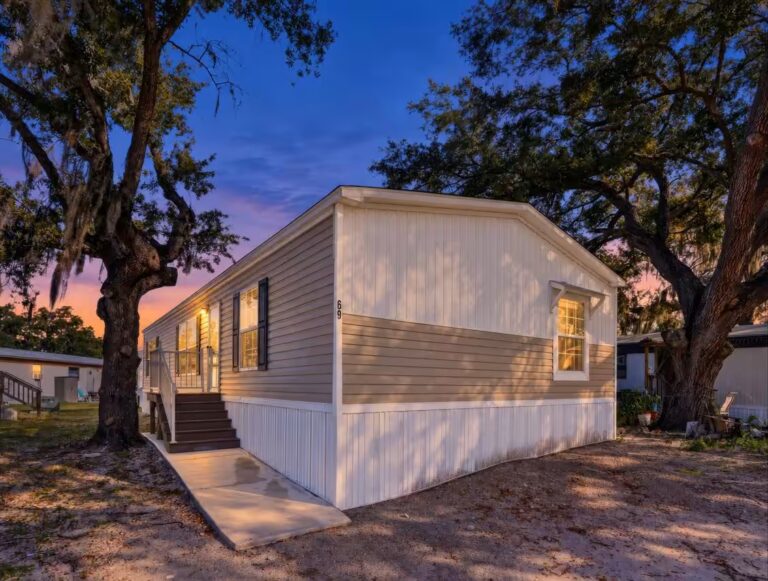 Mobile home 69 lit at dusk beneath moss-draped oaks, porch stairs leading to entrance